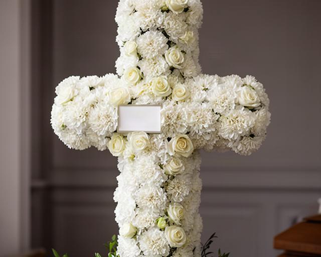 Cruz floral blanca formada con claveles y rosas en un espacio funerario sobrio
