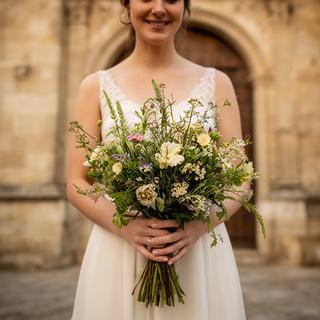 Novia sosteniendo un ramo silvestre frente a una iglesia de piedra en Andalucía
